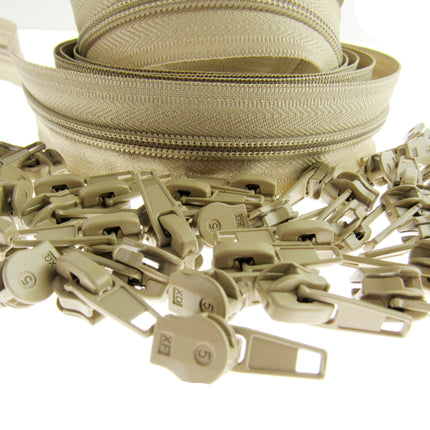 A close-up of a beige zipper with matching beige sliders and  pulls scattered in the foreground on a white background.