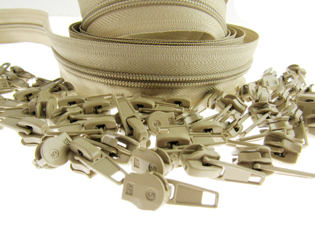 A close-up of a beige zipper with matching beige sliders and  pulls scattered in the foreground on a white background.