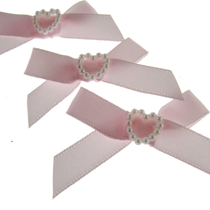 Three pink ribbons with pearl heart centers on a white background