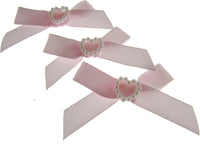Three pink ribbons with pearl heart centers on a white background