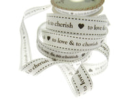Spool of ribbon with text 'to love & to cherish' on a white background