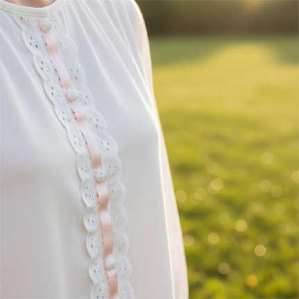 Close-up of white broderie anglaise insertion lace with pale pink satin ribbon woven through slotted eyelets on white blouse placket — Thread and Trimmings