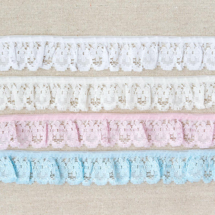 Four horizontal strips of decorative lace trim in white, cream, light pink, and light blue, laid flat on a beige textured fabric background.