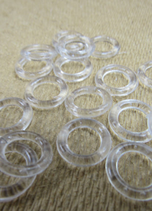 A collection of clear plastic Austrian blind rings scattered on a textured fabric surface.