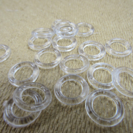 A collection of clear plastic Austrian blind rings scattered on a textured fabric surface.