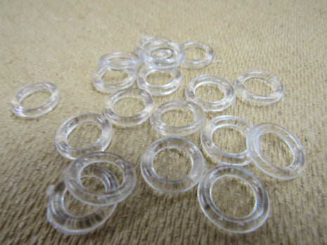 A collection of clear plastic Austrian blind rings scattered on a textured fabric surface.