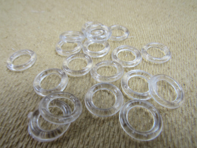 A collection of clear plastic Austrian blind rings scattered on a textured fabric surface.