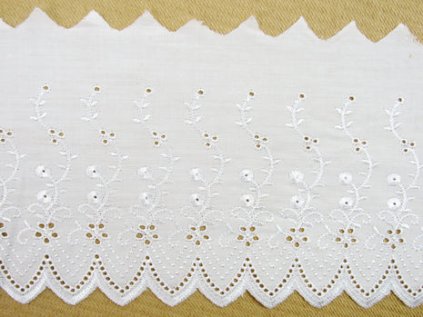 Flat white broderie anglaise fabric lace, 6 inches wide, with a pattern of small white flowers and dots, laid out on a flat surface.
