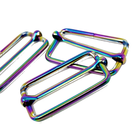Three metallic rectangular spring clips with an iridescent rainbow finish, arranged on a plain white background.