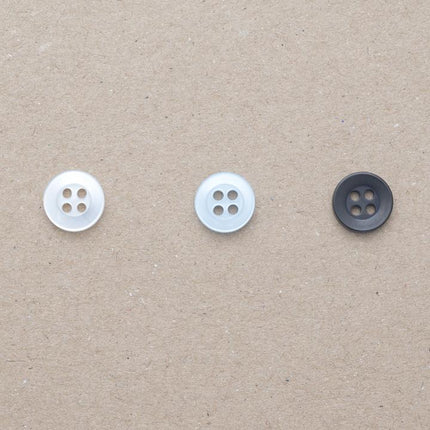 Four hole shirt buttons in black, pearl white and pearl light blue on a beige background