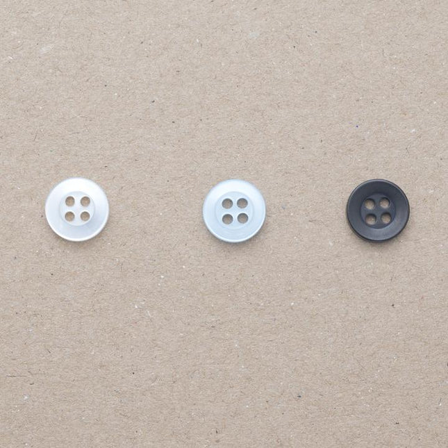 Four hole shirt buttons in black, pearl white and pearl light blue on a beige background