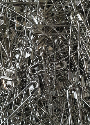 A close-up image of an assortment of nickel plated safety pins, showing their silver color and the looped end of the pins.