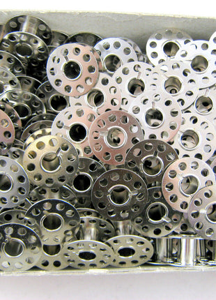 A collection of silver 15k sewing machine bobbins flat on both ends, with circular cut-outs in the centre.
