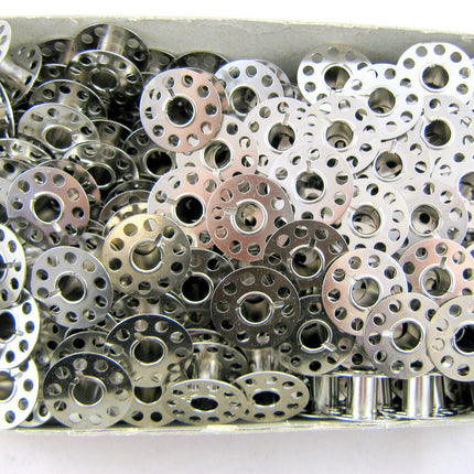 A collection of silver 15k sewing machine bobbins flat on both ends, with circular cut-outs in the centre.