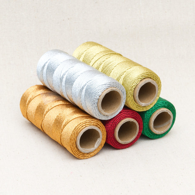 Five rolls of metallic lurex rope trimming in gold, silver, copper, red, and green colors, arranged on a surface.